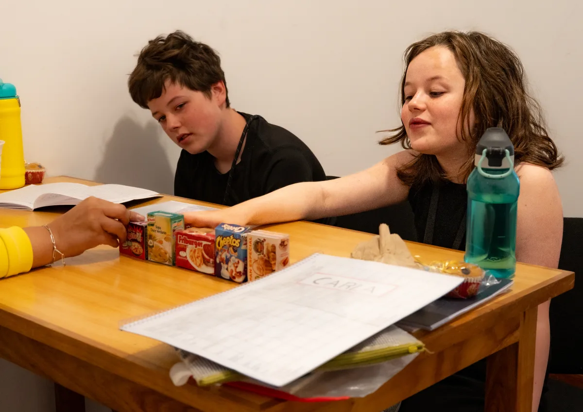 Students learning Spanish with mini cereal boxes at a table